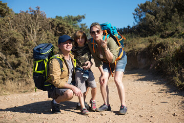 Happy mid adult parents hiking with son outdoors. Family backpackers embracing, looking at camera and smiling. Active family weekend concept