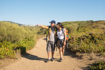 Backpacker pointing at view to his daughter. Man hiking with teen daughter in mountains in summer. Active family weekend concept