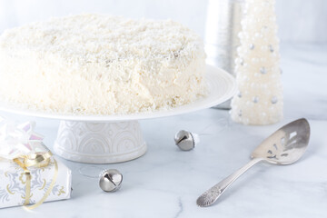 A coconut covered white frosting cake surrounded by white decorations.
