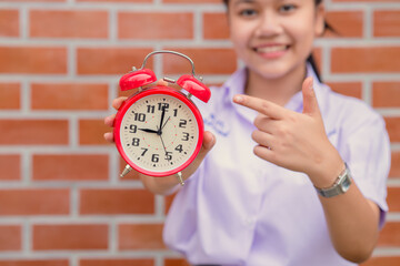 happy Asian school teen girl smiling hand pointing at alarm clock for times to awake to education...