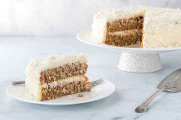 A coconut covered carrot cake with one slice in front ready for eating.