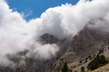 Panoramic view of the cloud covered slopes and rocky ridges of Pieria Mountains near Mount Olympus in Mt Olympus National Park, Thessaly, Greece, Europe. Trekking on hiking trail through mystical fog