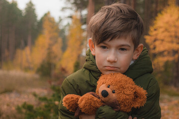 Child alone in the forest with a teddy bear. A boy in solitude in an autumn forest