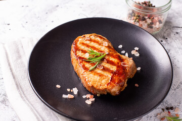 Juicy grilled beef steak with spices and rosemary on black plate on grey textured background.