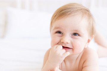 laughing or smiling baby boy blond with big eyes with a finger in his mouth close-up or portrait in a crib at home, the concept of children's goods and accessories