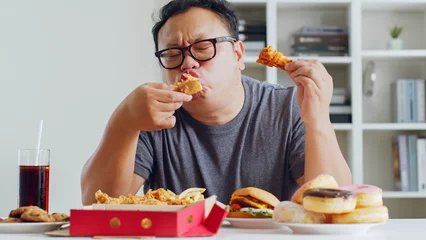 Rolgordijnen Asian fat man enjoy to eat unhealthy junk food, hamburger, pizza, fried chicken © Nattakorn