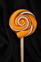 Handmade hard candy lollipop swirl in Halloween colors of orange and black on a wooden stick - 538639364