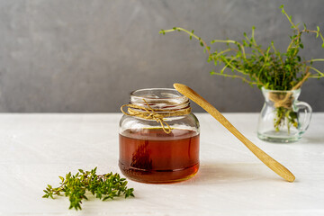 Thyme honey in small glass jar with wooden tea spoon, small thyme branch on white wooden table with...
