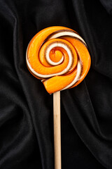 Handmade hard candy lollipop swirl in Halloween colors of orange and black on a wooden stick - 538640156