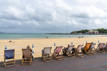 people relaxing in lounge chairs on the esplanade at Weymouth Beach in Dorset - obrazy, fototapety, plakaty