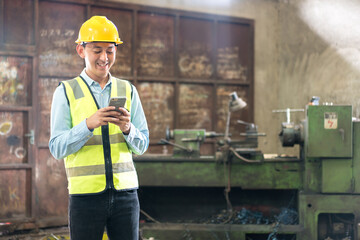 Portrait of industrial worker indoors in factory. Manual workers discussing while using smart phone at factory. Smiling and happy employee.