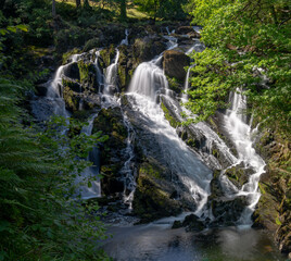 the Swallow Falls waterfall in Anglesey in northern Wales surrounded by lush green summer vegetation