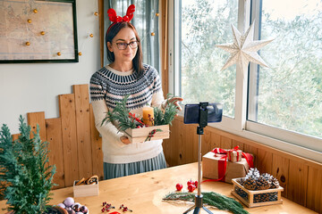 Female florist blogger making winter ikebana with fresh pine branches, candle and christmas...