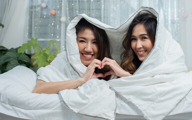 Two asian women laying down under blanket and staying on bed at home showing LGBT Concept..