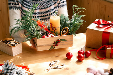 Woman's hands making christmas arrangement. Female florist creating winter ikebana with fresh pine branches, candle and christmas decorations. Small business. Seasonal winter workshop.