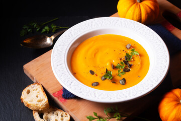 Food concept Organic pumpkin soup on wooden board and black slate stone background with copy space