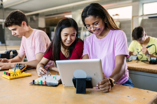 Group Of Diverse Teenage Students Learning Together To Build Electronic Circuits At High School - Asian And African American Female Classmate Working At Technology Class
