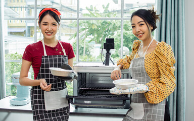 Two Asian beautiful adorable women or friends wearing aprons, smiling with happiness, doing...