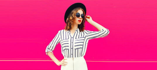 Beautiful young woman model wearing white striped shirt, black round hat, skirt on pink background