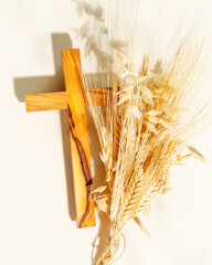 Wooden crucifixion with bouquet of wheat and rye on light background. Religion card suitable for...