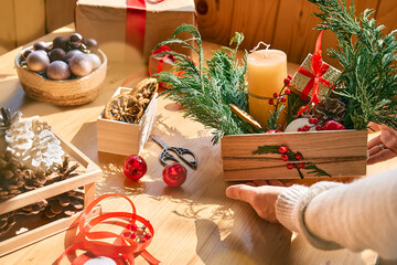 Woman's hands making christmas arrangement. Female florist creating winter ikebana with fresh pine branches, candle and christmas decorations. Small business. Seasonal winter workshop.