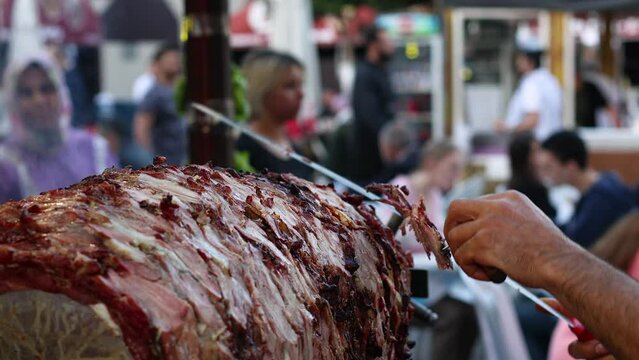The chef prepares a doner kebab by slicing toasted meat slices from outdoor skewers.
