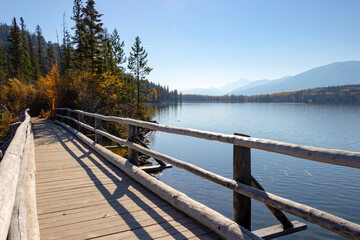 Fototapeta na wymiar scenic lake with mountains in background and wooden bridge walkway in foreground during autumn