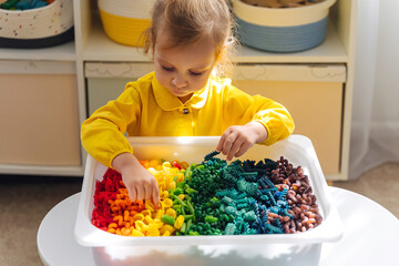 Child playing with sensory bin with dried pasta in rainbow colors. Dyed pasta for play and craft...