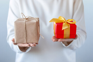 Close-up of female hands holding a gift boxes in different designs. Box kraft paper and tied jute and a gift box with a yellow bow. Concept of choice, sustainable consumption, ecology, contrasts.