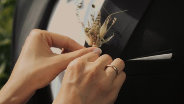 Groom puts on a boutonniere. A girl, a bride or bridesmaid, straightens a flower buttonhole on a man's suit. bow tie bride . slow motion