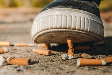 A man puts out a cigarette with his foot. The shoe steps on the cigarette butts. Smoking is injurious to health. Cigarettes