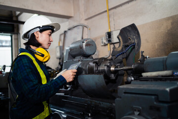 A female mechanical engineer or mechanic in a safety uniform checks the readiness of a lathe inside an industrial plant. Asian female engineer working in an industrial plant.