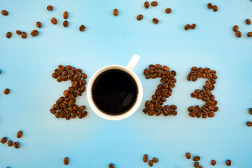 2023 number made of coffee beans and cup of coffee on light blue background as symbol of new start, goals and beginning. Happy New Year and Merry Christmas.