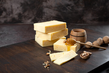 Hard cheese on a dark background. Cheese with honey and nuts.