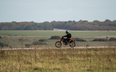 Obraz premium motorcyclist riding an off-road motorbike along a stone track, crossing open countryside in sunshine