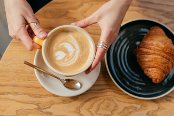 girl's hands with a cup of coffee and a croissant