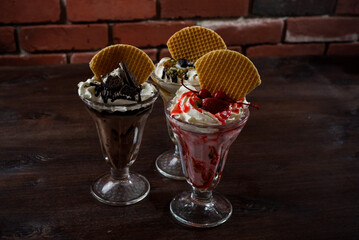 Three milkshakes in tall glasses with waffles, whipped cream cherries blueberry and chocolate flavors.