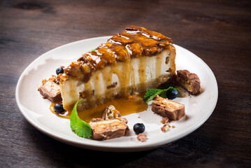 Caramel-flavored cheesecake. A slice of dessert topped with salted caramel syrup, peanuts and milk chocolate. The cheesecake is garnished with blueberries and mint leaves.