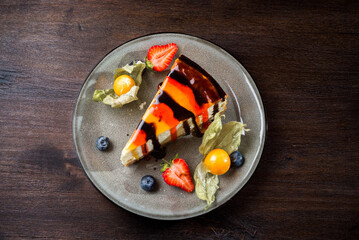 Delicate creamy cheesecake with chocolate and strawberry syrup. Piece of cake on a plate with fresh strawberries, blueberries and physalis.