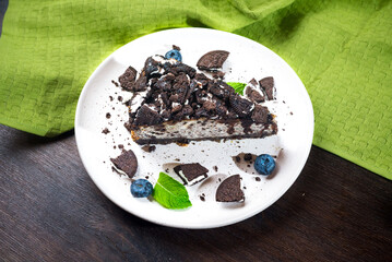 Cheesecake with brown cookies, blueberries and mint. Dark brown cookie dessert portion with chocolate topping.