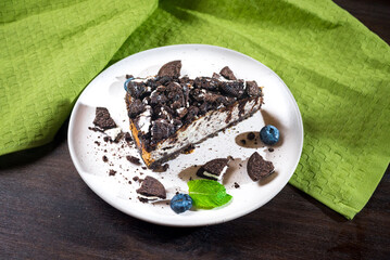 Cheesecake with brown cookies, blueberries and mint. Dark brown cookie dessert portion with chocolate topping.