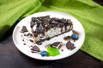 Cheesecake with brown cookies, blueberries and mint. Dark brown cookie dessert portion with chocolate topping.