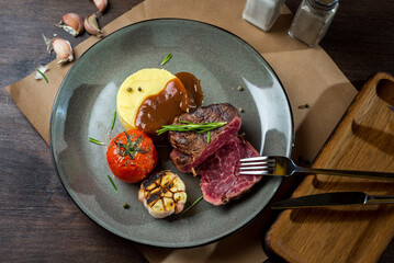 Filet mignon with mashed potatoes and grilled tomato and garlic on a plate with rosemary sprigs. A...