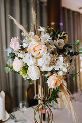 Flowers, reeds, wild flowers stand in a metal vase on a table in a restaurant, as a decoration. Close-up wedding photography.