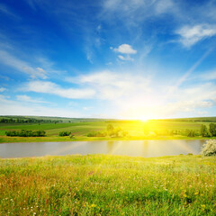 Meadow, lake, agricultural fields and sunrise on blue sky.