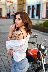 Fototapeta na wymiar Young beautiful woman shows her bare shoulder with a tattoo standing by a bike on the street