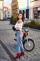 Obraz na płótnie Canvas Young beautiful woman in unbottend shirt with a tattoo on her shoulder standing by a bike on the street