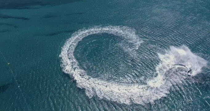 Aerial Top Down View Shot of a Person Jet Skiing in Circles. Beautiful Blue Oceanic Waters and Sun is Shining. 
