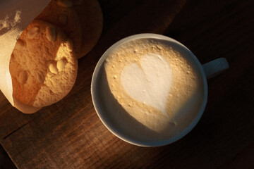Cappucino with cookies on a wooden surface under sunlight