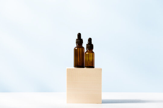 Serums in dark glass dropper bottles on wooden cube podium at blue backgroind. Organic cosmetics. Skin care beauty concept